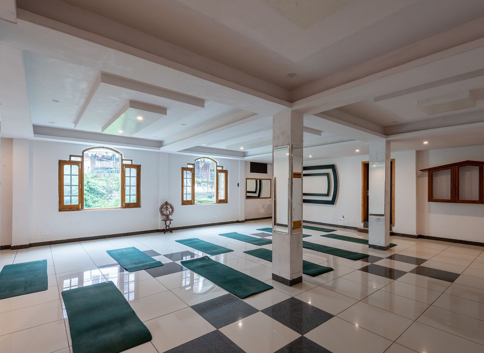 A spacious yoga studio with a tiled floor, large windows, and multiple green yoga mats laid out - DLS Meghavan Resort
